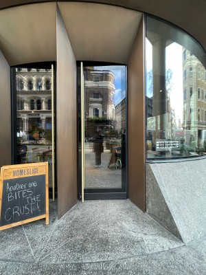 Facing glass door with black frames. Pull to open metal handle on left.