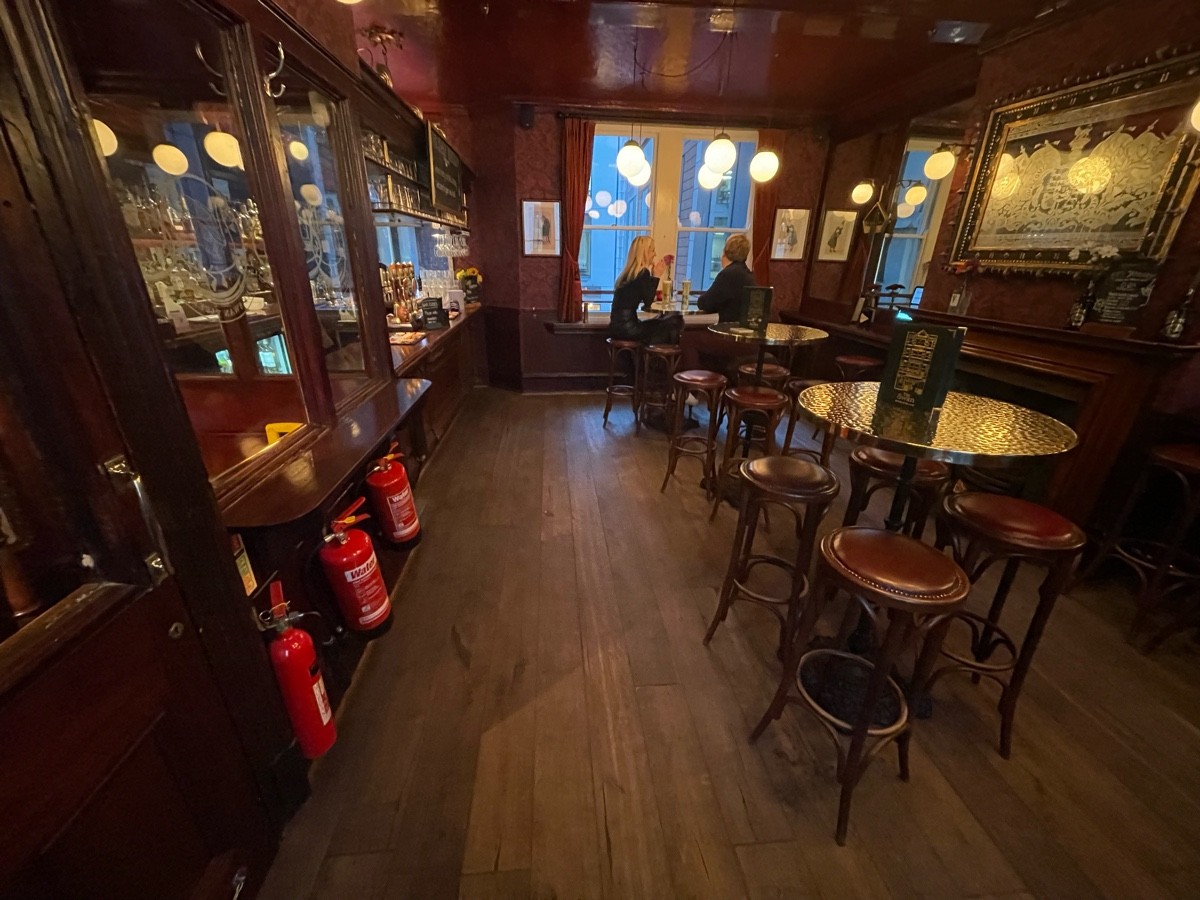 From doorway facing left. High table on left, bar counter following. High tables and stools along right.