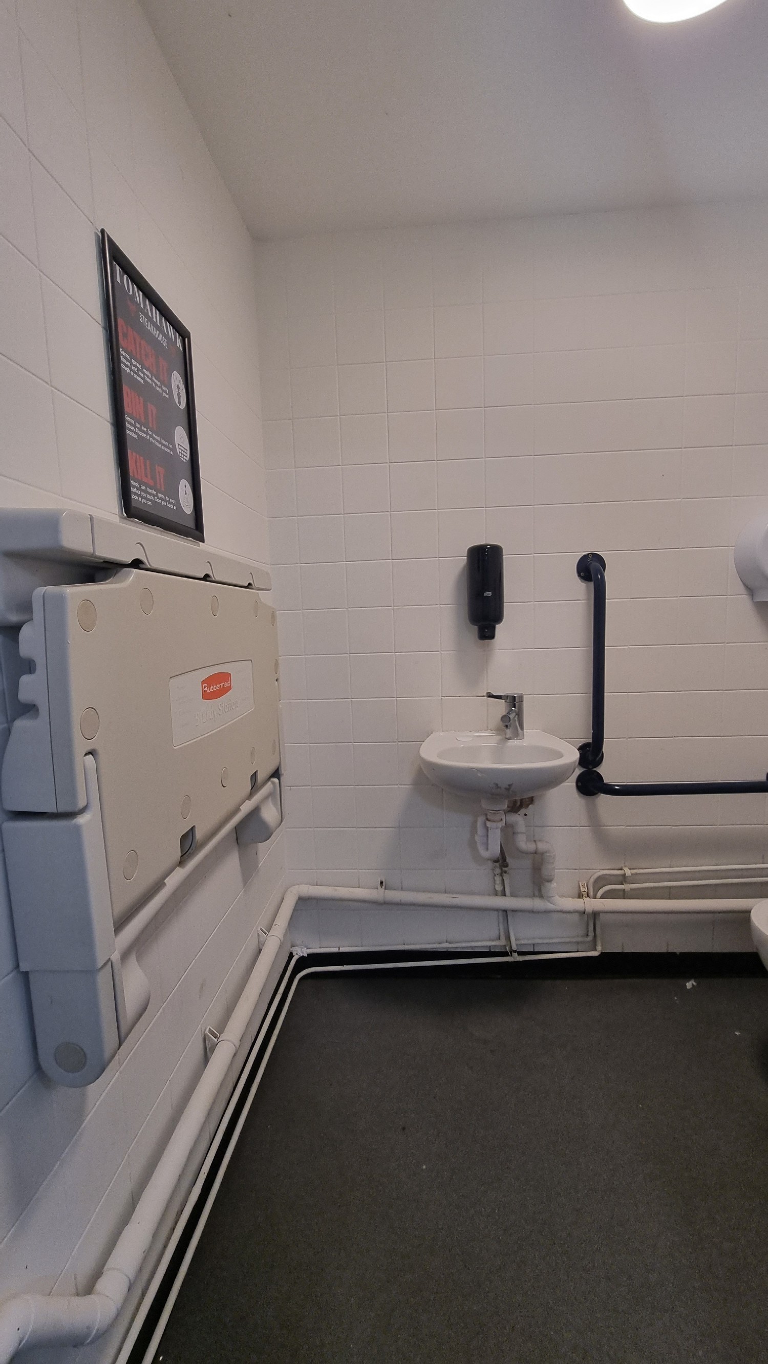 Baby change unit on left side wall and sink in the middle of photo and grab rail on right side.