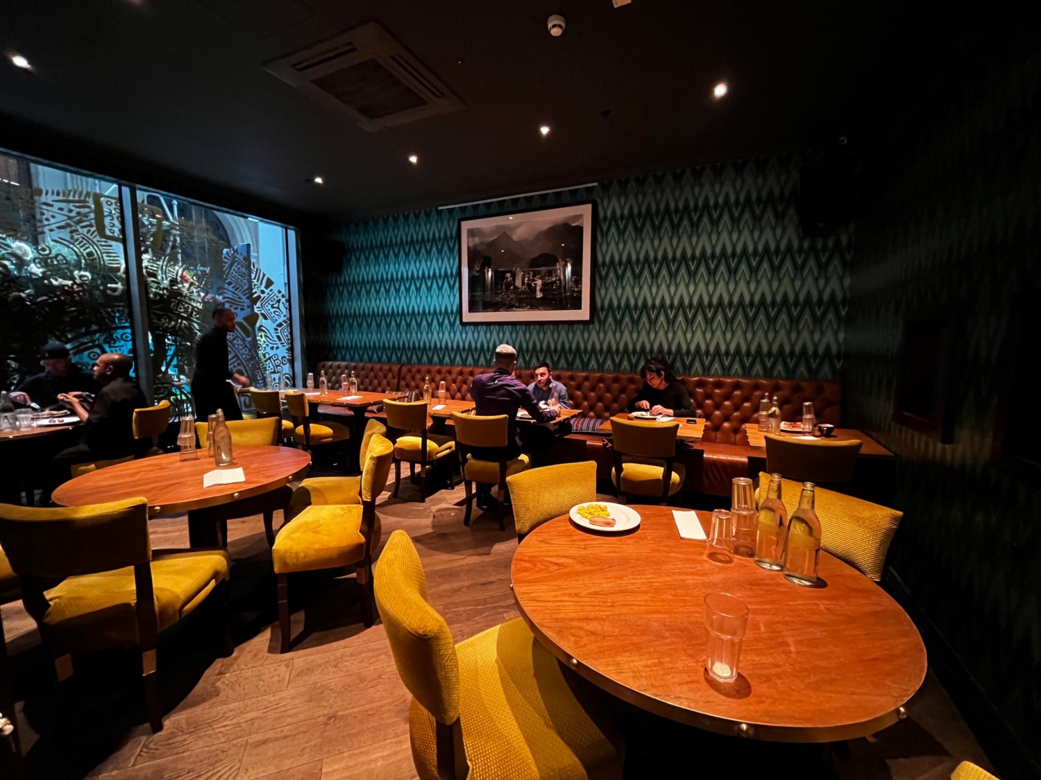 Private area behind curtain from curtain doorway. Round tables with chairs followed by bench on back wall providing seating to tables with chairs.