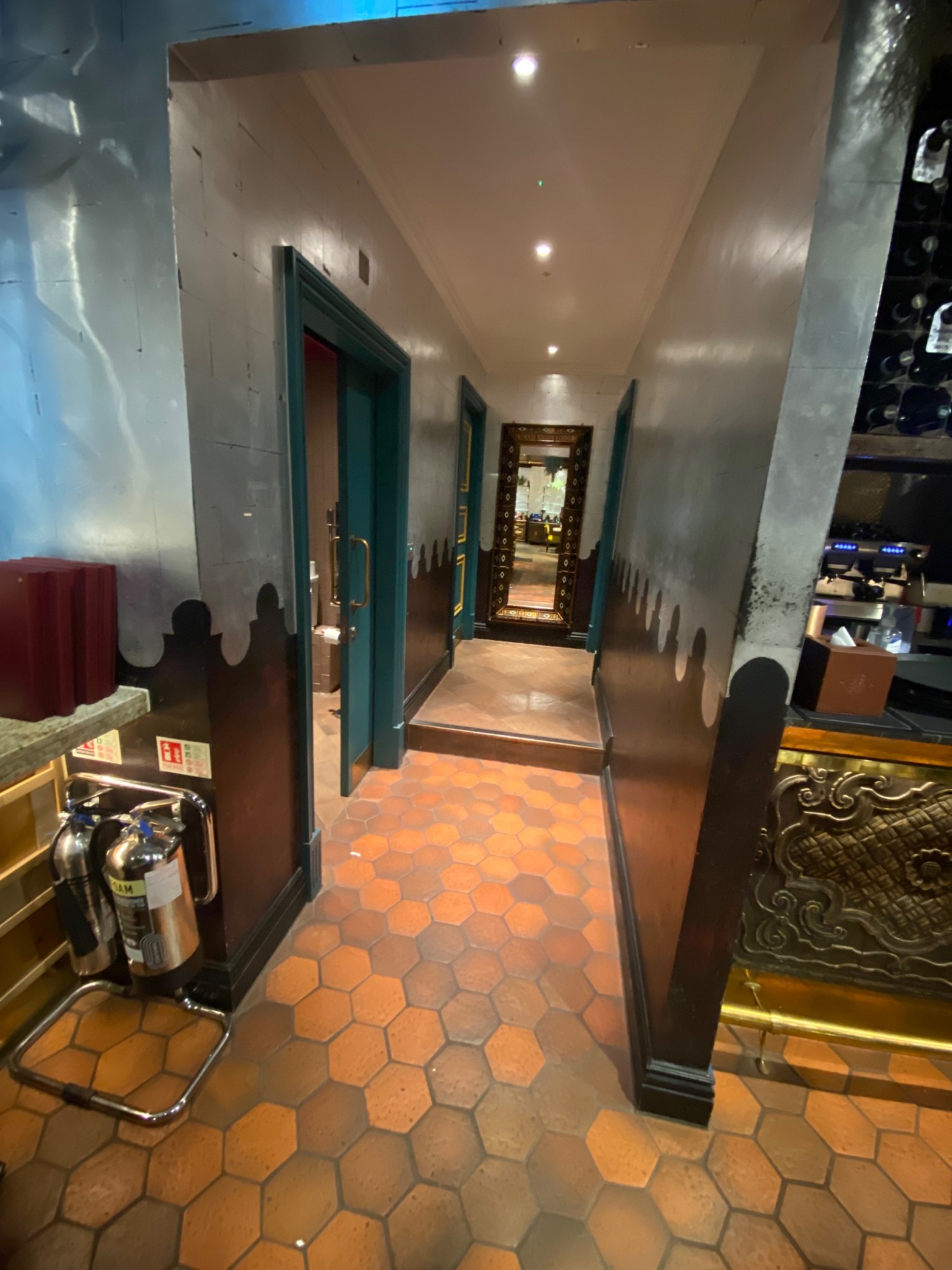 Left of bar facing straight ahead. Wide corridor. Door to bathroom to left.