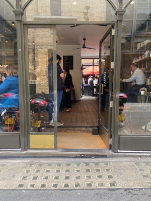 Glass door with metal frame and metal handle. Push from left to open. Step up before door, followed by doormat and another step up.