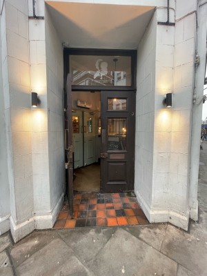 Facing brown wooden double doors with glass panels. Pull brass handle on left door to open.