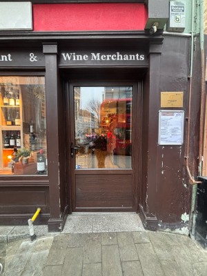 Glass door with wooden frame ahead. Push black metal handle at left of door to enter.