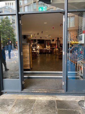 Main entrance along Crutched Friars. Grey framed double glass push doors with handles in middle. Three steps to access.