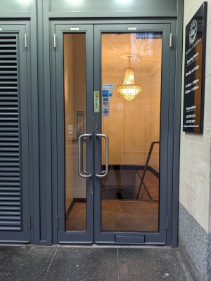 Glass door with grey frame and metal handle. Pull from centre to open.