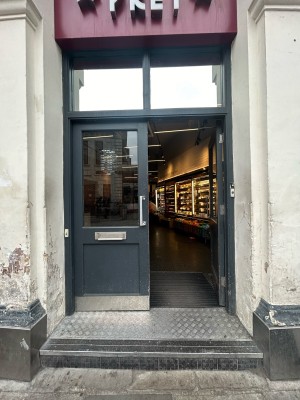 Double dark grey wooden doors with glass panel. Push silver handle in middle to open. White doorbell with grey button on left of door.
