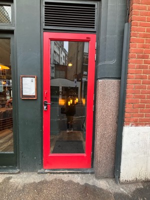 Glass door with red wooden frame ahead. Pull metal handle at left to open.