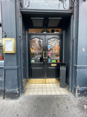 From sidewalk facing venue. Glass door with black frames. Pull brass handles in center to open.