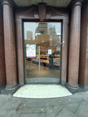 Facing glass door. Push silver metal handle on left to open.