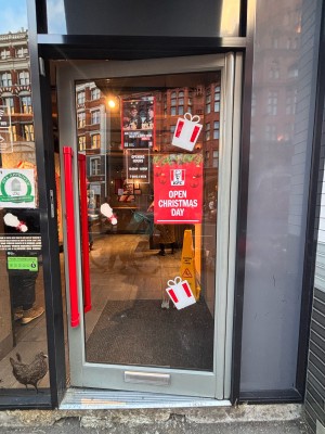 Glass door with grey frame ahead. Push red metal handle at left to open.