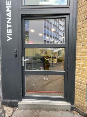 From sidewalk facing venue. Glass door with black frame. Push to open metal handle on left.