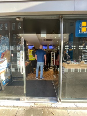 Facing glass door. Push to open metal handle on left.