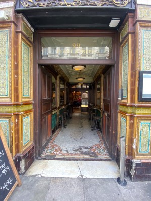 First set of dark wooden doors. Push from middle to open. Outdoor seating beyond, path in centre to second doors at back.