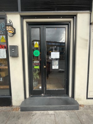 Large step, followed by a small bump leading up to single door. Push door open from the left.