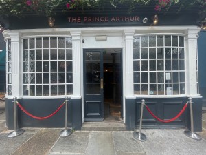 From street looking straight. One step up. Wide double doors. Glass and grey. Push in centre.
