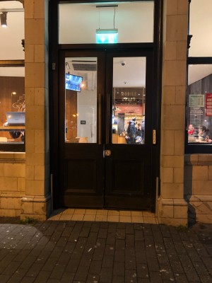 Black wood and glass panelled doors. Pull wooden handles in centre to open. White doorbell to right of doors.