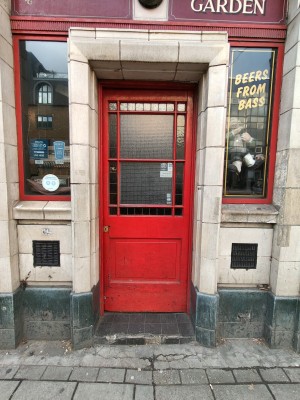 Facing red framed frosted glass panelled door. Push from left to open.