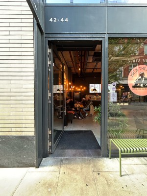 Single glass door with dark grey frame. Silver vertical metal handle along right. Push to open.