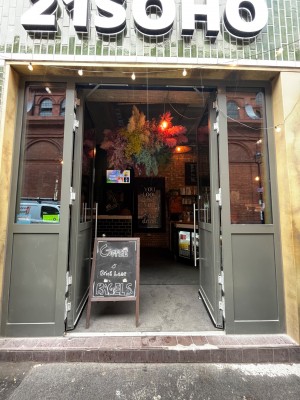 Grey-framed glass double push doors with handles in middle. Sign partially obstructing entrance on left. Step & small bump along door.