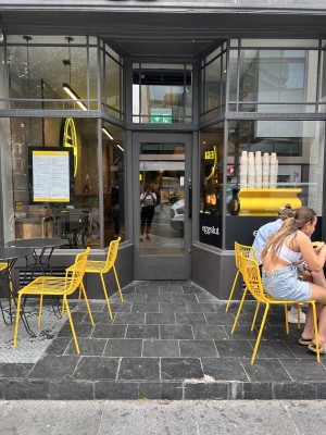 From street, black platform with step with outdoor seating on to left and right of path to door. Door set back from the front.