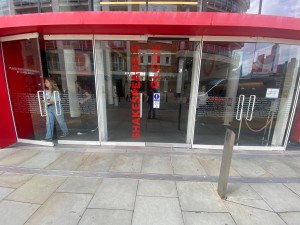 Facing glass doors with red frame. Push button on right to open.