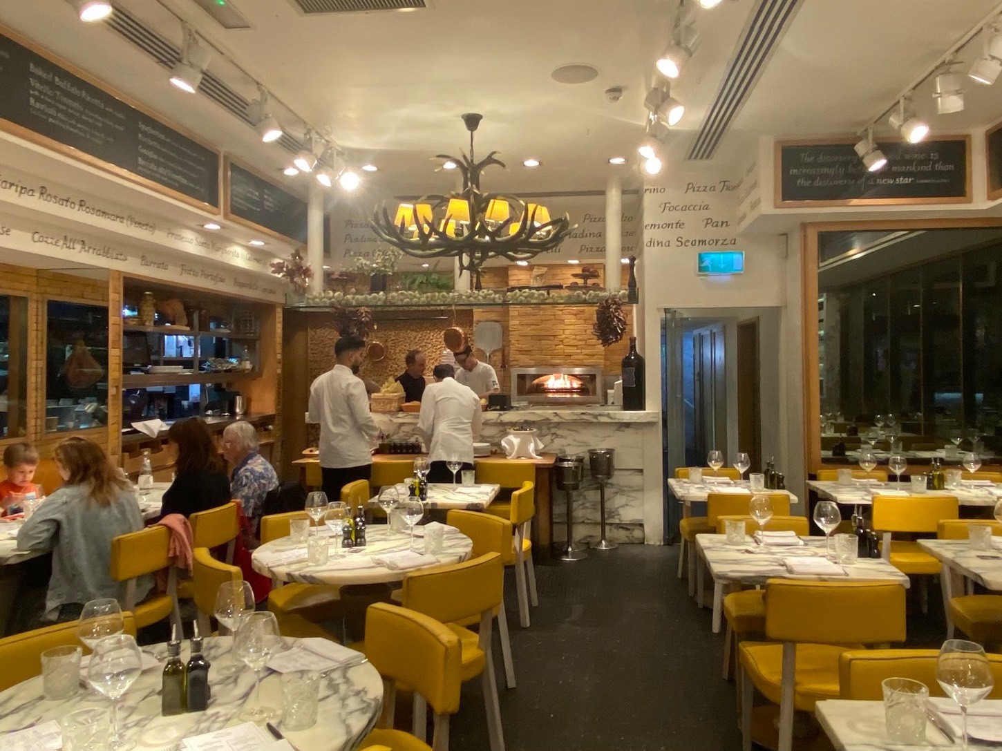 Looking straight from further down middle of main area. Open kitchen to the back, tables & chairs on the right, tables & chairs & half booths on left.