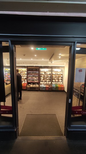 Glass doors with grey frames ahead. Push in centre to open via metal vertical handle.