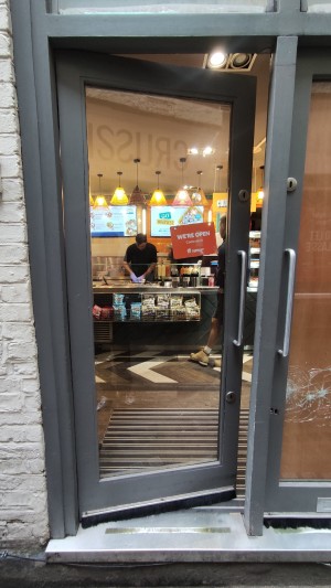 Glass door with grey frames ahead. Push via vertical metal handle on right to open.
