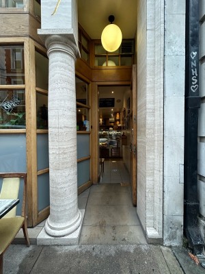 Single glass door with light wooden frame. Pull silver metal handle right to open. Stone pillar on left.