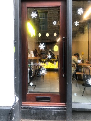 From sidewalk facing venue. Glass door with brown frame. Push to open handle on right.