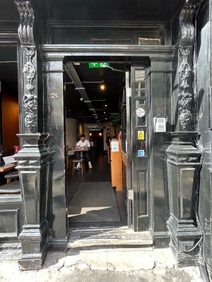 Wooden black door with gold handle on mid left. Push to open.