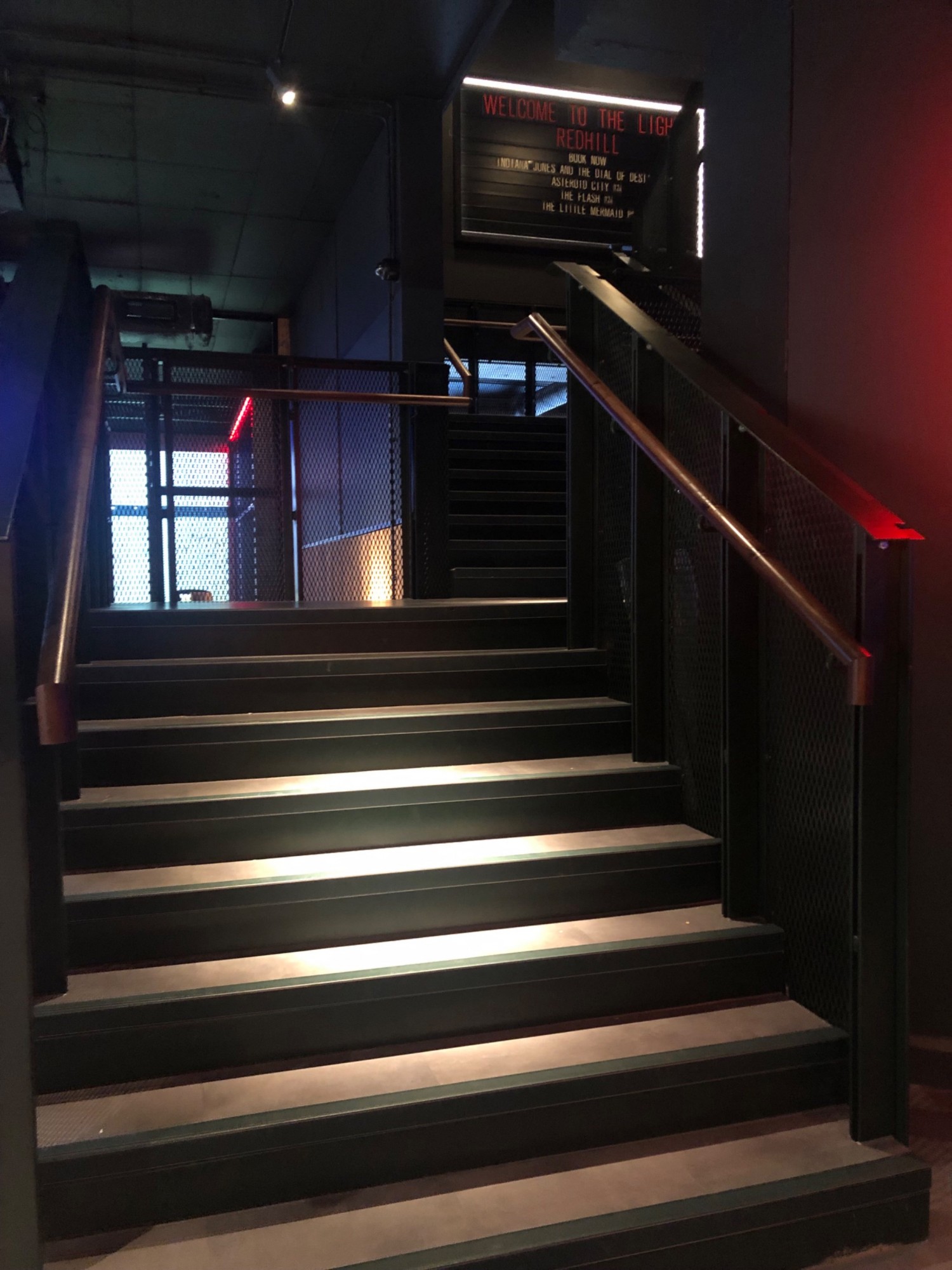Dark wide stairs up from foyer to cinema and mini golf. Steps have light colour contrast. Handrails on left and right.