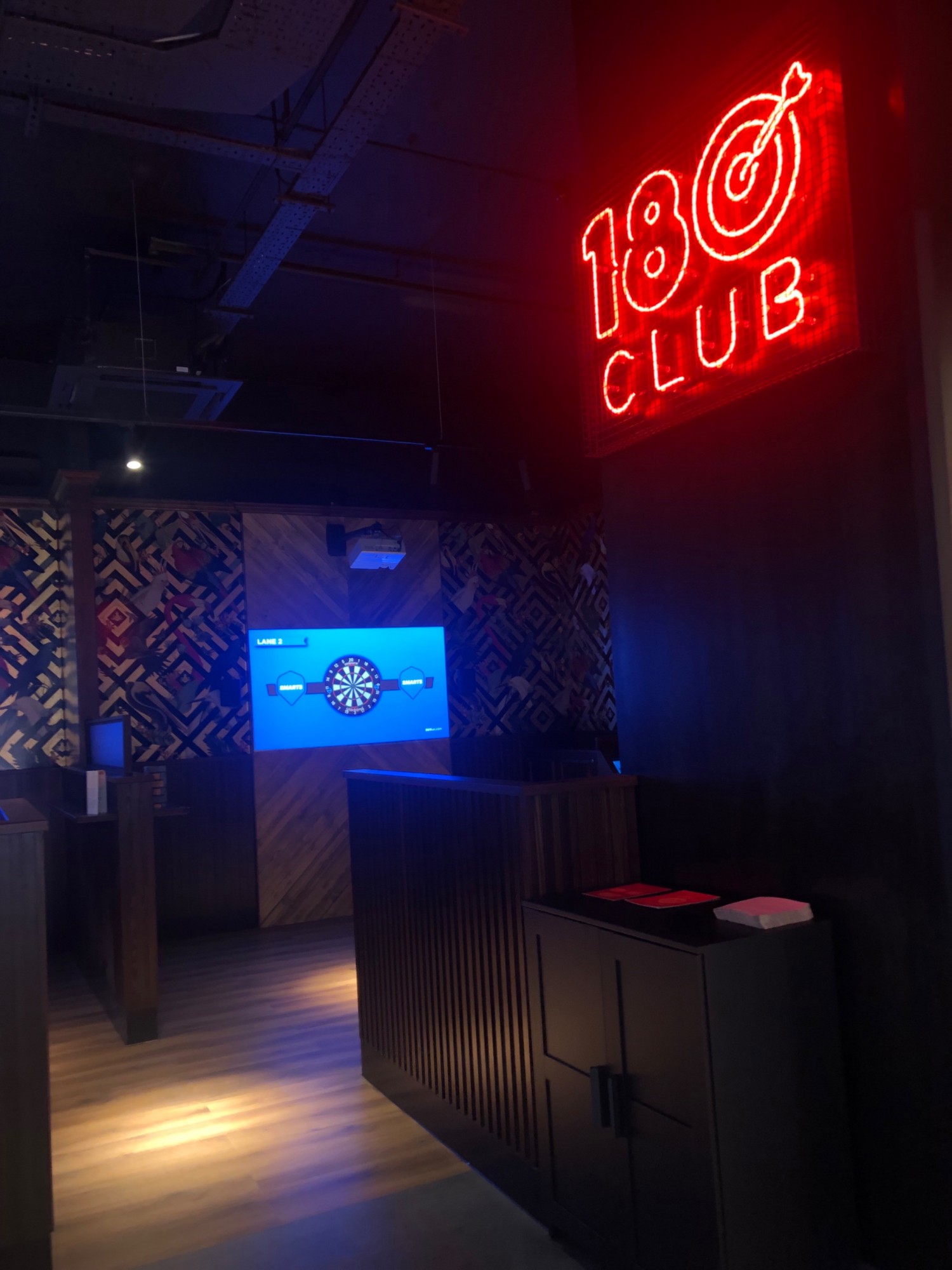 Dark room with neon signs and screen for digital darts game.