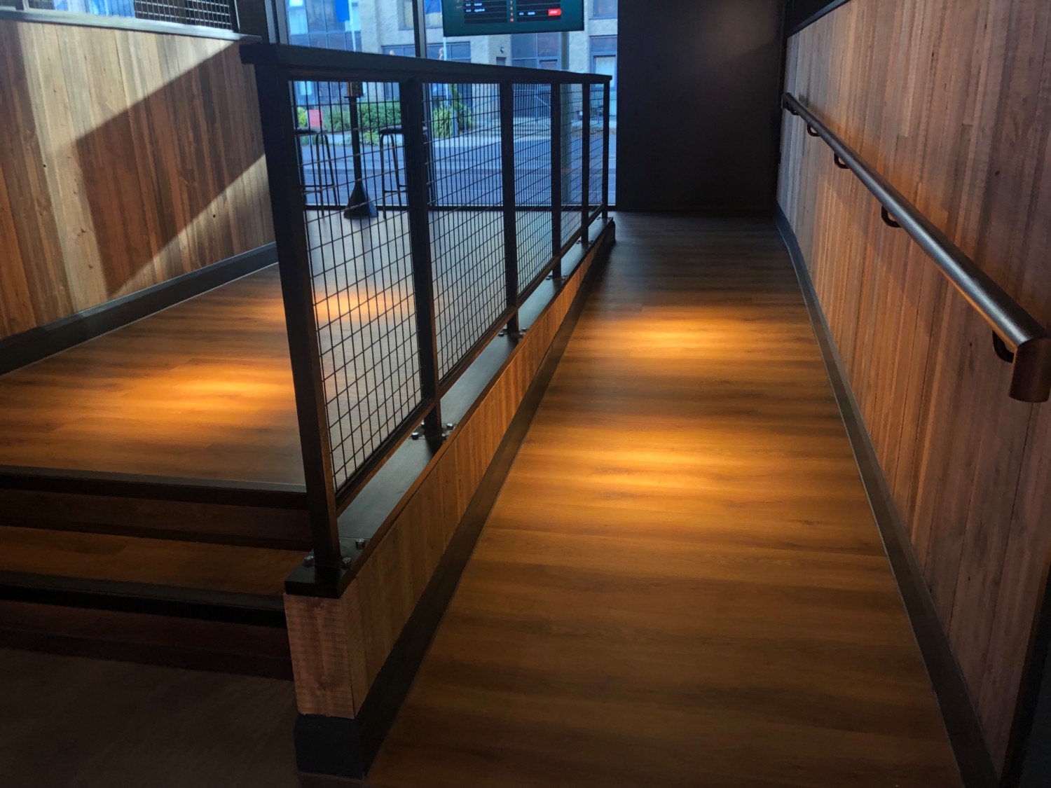 Wooden flooring steps on left and ramp on right from arcade to bowling area. Black contrast edges to steps, ramp and handrails.