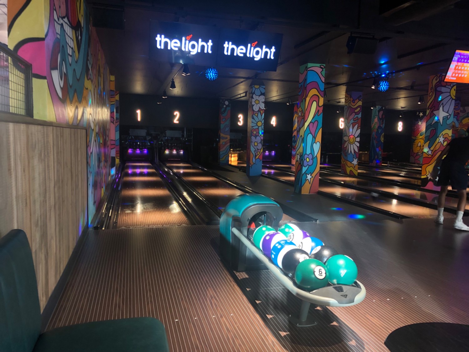 Blowing alley with neon lighting and busy decor, wooden flooring.