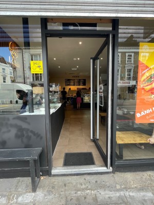 From sidewalk facing entrance. Black framed glass door ahead. Push door from left to open inwards.