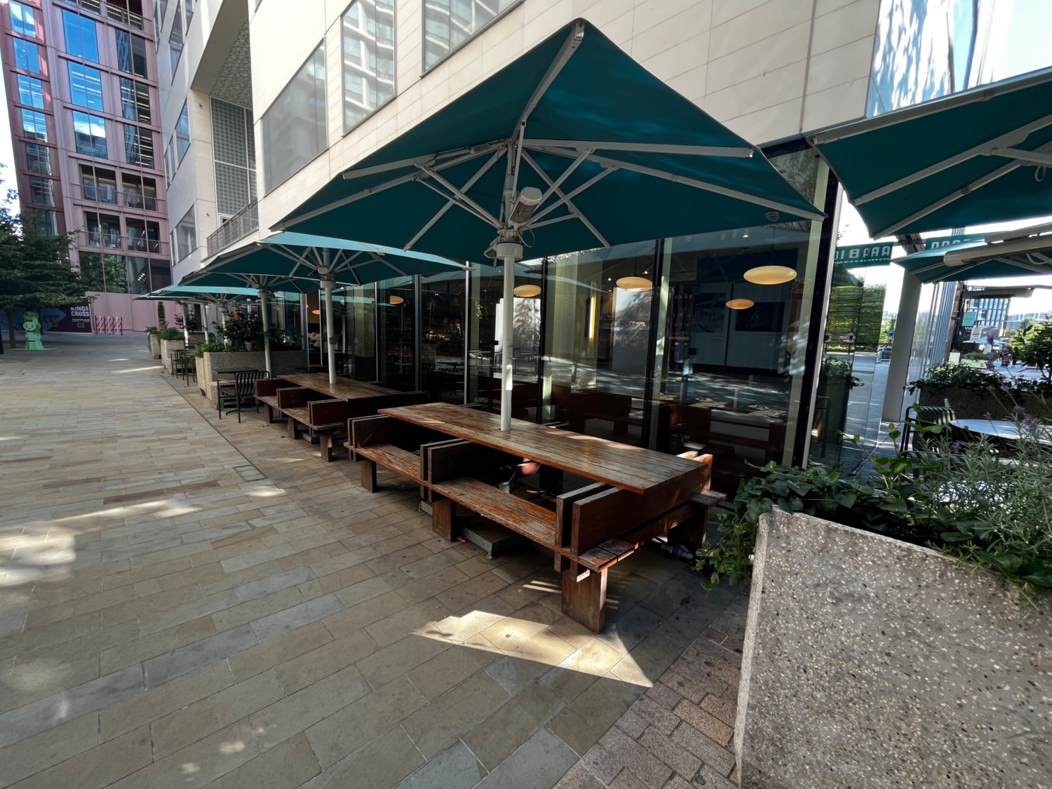 Outdoor area on left of venue. Integrated tables and benches on outer wall, tables with chairs further along. Area continues along outer wall.