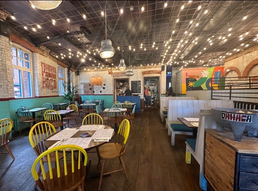 From display table, looking right. Tables and chairs spread on left. Display table on right. Booths behind.