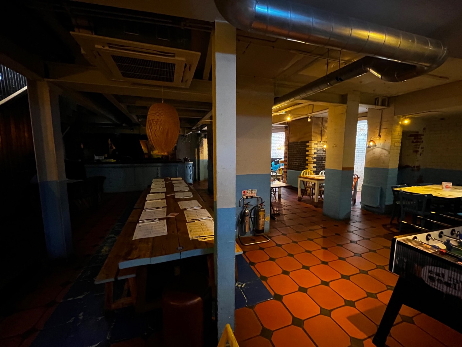 Downstairs area to left. Long table with benches on left. Football table on right. Area continues ahead, to left, and right.