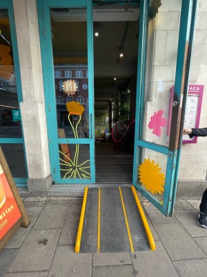 Glass doors with blue frame. Pull metal hands in centre to open. Ramp upon request at the entrance bottom.