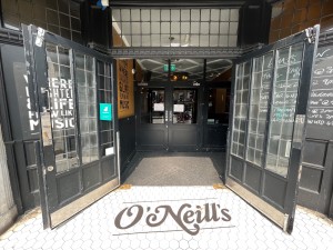 Black wood doors with glass panels and metal handles in centre. Pull to open. Doormat after doors.