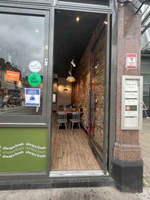 Glass door with grey frame ahead. Push handle on the left to open.