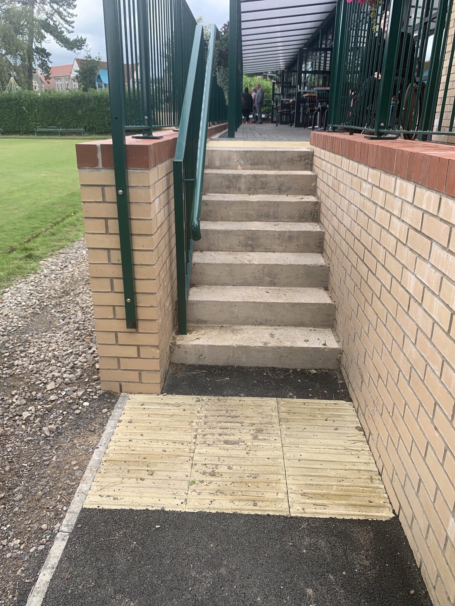 Raised, colour contrasted tiles at bottom and top of stairs. Meter high grab rails on left of stairs coming up.