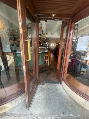 Glass door with wood frame indented on left side of venue when facing storefront. Pull from right to open. Small bump at foot of door.