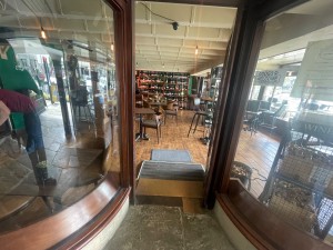From the street looking straight. Glass door with handle in the centre right. Push to open.