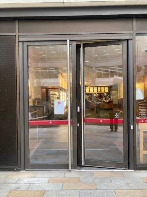 Glass doors with metal frame ahead. Push doors to open via handles in center. White doorbell for assistance to the right of doors.
