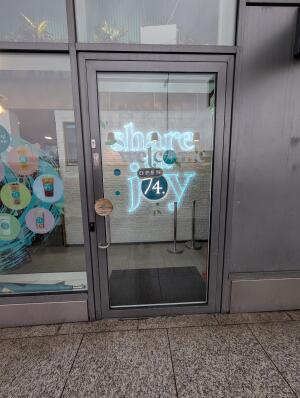 Grey frame glass door in front. Silver handle on left. Push to open. Doorbell for assistance on left.