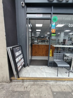 Grey framed glass door. Push grey handle on right to open. Outdoor seating on right.