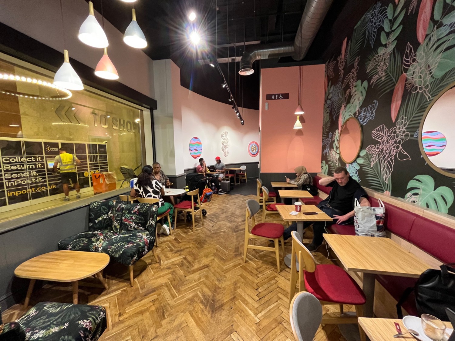 From archway looking ahead. Lounge on left. Chairs and table along left wall. Pathway ahead leading to bathroom at back. Half booths along right wall.